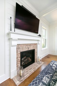 a flat screen tv mounted above a fireplace in a living room with hardwood floors and white walls