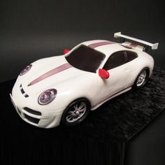 a white sports car cake sitting on top of a black tablecloth covered countertop