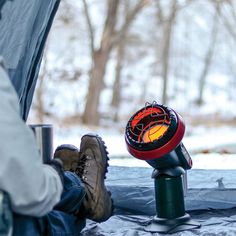 a person sitting in a tent with their feet on the ground next to a stove