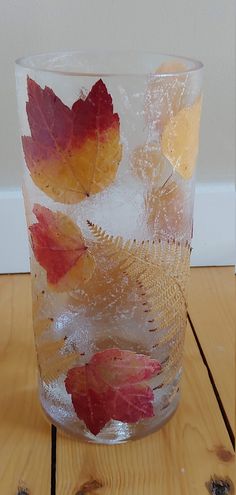 a glass filled with leaves sitting on top of a wooden table next to a wall