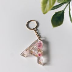 a glass letter keychain with pink flowers on it and a green plant in the background