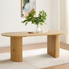 a wooden table sitting on top of a white rug next to a painting and vase