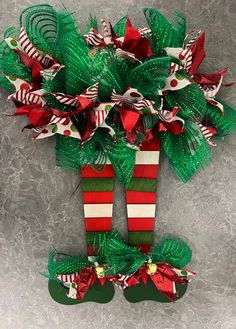 a green and red christmas decoration hanging on the side of a wall in front of a gray background