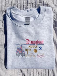 Item Description: Crewneck Featured in an ash color with embroidered Classic Disneyland ticket inspired design in pink blue and gold lettering . Perfect for a day at the park Gildan unisex pullover sweatshirt/Crewneck made out of 50/50 cotton and polyester blend. Size Recommendations: For women -True to size -For an oversized look size up one size For men -For relaxed look size up Recommended wash: -Machine wash cold -Inside out  -Tumble Dry Low Return Policy: -All sales are final. No returns, no exchanges due to t-shirts are being made to order, but please feel free to contact us for any problem or questions. Disneyland Shirt, Disneyland Tickets, Disneyland Shirts, Embroidered Crewneck, Gold Lettering, Sweatshirt Crewneck, Disney Outfits, Ash Color, Disney Trips