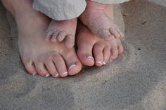 two people standing on the sand with their feet covered in sand and white nail polish