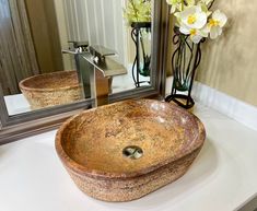 a bathroom sink sitting under a large mirror next to a vase with flowers in it