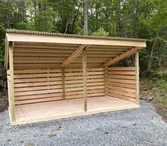 a wooden carport in the middle of a forest with lots of trees behind it