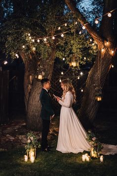 a bride and groom standing in front of some trees with lights strung from the branches