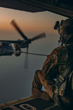 a man sitting in the back of a helicopter next to a helicopter flying over water