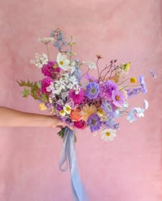 a person holding a bouquet of flowers on a pink background with a blue ribbon around it