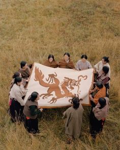 a group of people standing around a large flag in the middle of a grass field