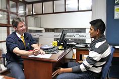 two men sitting at a desk talking to each other