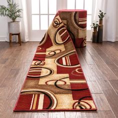 a red and beige area rug on the floor in front of a window with potted plants