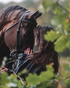 a woman is hugging a horse in the woods with her hand on it's face