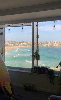 a surfboard leaning against a window in a living room with the ocean and city seen through it