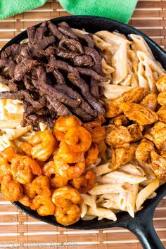 a skillet filled with meat, pasta and other foods on top of a bamboo mat