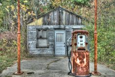 an old rusty gas pump in front of a run down building with trees around it