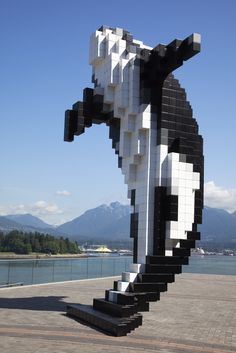 a large black and white dog sculpture on the side of a road next to a body of water