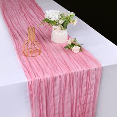 a pink table runner with white flowers in vases next to it on top of a table