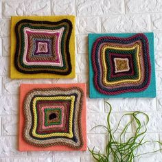 three crocheted squares are hanging on the wall next to a potted plant