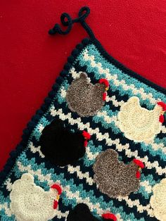 a crocheted square with roosters on it sitting on a red tablecloth