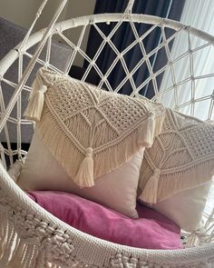 a white hanging chair with pink pillows and tassels