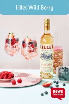 there are three wine glasses with strawberries on the table next to each other and two bottles