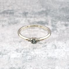 a white gold engagement ring with two diamonds on the side, sitting on a gray surface