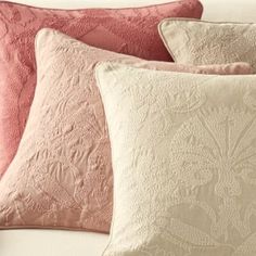 four pillows are lined up on a bed with white sheets and pink throw pillows in the background