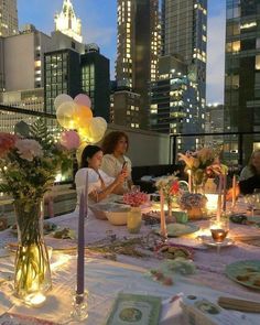 two women sitting at a table with plates and candles in front of the city skyline