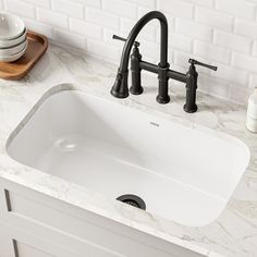 a white sink sitting under a faucet next to a wooden cutting board on top of a counter