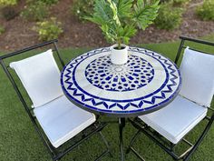 a small table with two chairs and a potted plant on it in the grass