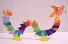 an origami dragon made out of colored paper sitting on a table next to a white wall