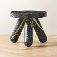 a black and white marble table with three legs on top of it, sitting on a wooden floor