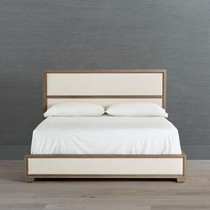 a bed with white sheets and pillows in a room that has wood flooring on the side