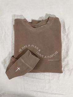 This 'He Has a Plan and I Have a Purpose' embroidered sweatshirt is embroidered in a wave and features 'Jeremiah 29:11' below it. It's the perfect Christian sweatshirt to wear for Easter, on Sundays, or any day. You'll find yourself reaching for it because it's SO cozy and it even passes the aesthetic vibe with the vintage pigment-dyed look. Example photo pictured on pigment clay with ivory thread and the cross upgrade for the wrist. Standard unisex sizing. For women, ordering your normal size will be relaxed and sit at the hips. For an oversized look, size up one (or two if you like really oversized). Trendy Christian Shirt, Jeremiah 29:11 Sweatshirt, Christian Tops For Women, Bible Verse Crewneck, Sweatshirt Inspo Aesthetic, Christian Shirts Designs Aesthetic, Oversized Christian Shirts, Embroidery Cross Christian, Christian Embroidery Sweatshirt