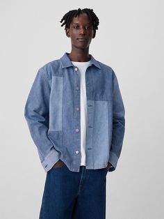 a man standing in front of a white wall wearing a blue jean jacket and jeans