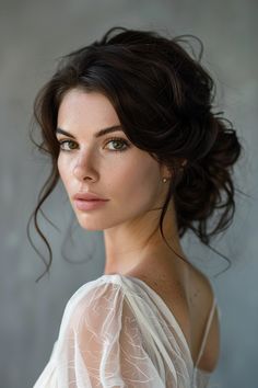 a woman with dark hair wearing a white dress and posing for a photo in front of a gray wall