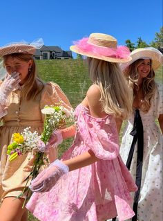 three women in dresses and hats walking down the street with flowers on their bouquets