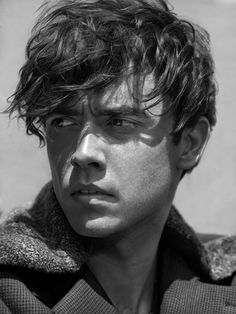 black and white photograph of a young man with curly hair wearing a coat looking at the camera