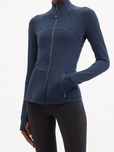 a woman wearing a blue jacket and black leggings with her hands on her hips