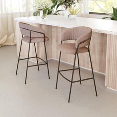 two bar stools sitting next to each other in front of a counter with potted plants on it