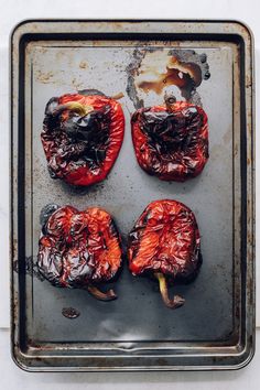 four red peppers on a baking sheet ready to go in the oven for roasting