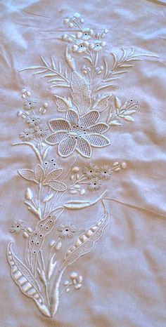 an embroidered sheet with flowers and leaves on the bottom is laying on a tablecloth