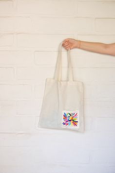 a person holding a white bag with colorful designs on the front and side, against a white brick wall