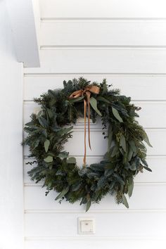 a green wreath hanging on the side of a white building with a brown ribbon tied around it