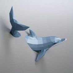 two origami whale sculptures hanging on the wall in front of a gray background