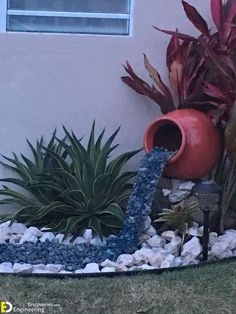 a water fountain in the middle of a garden with plants and rocks on the ground