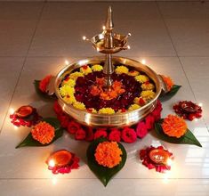 a metal tray with flowers and candles on the floor in front of it, surrounded by leaves