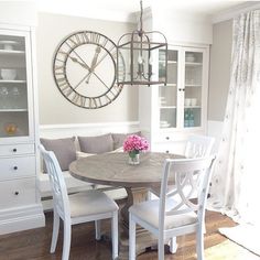 a dining room table and chairs with a clock on the wall above it in front of a window